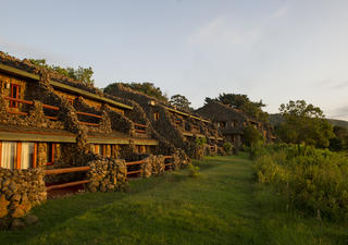 Das Äußere der Ngorongoro Serena Safari Lodge ist ein Triumph der Verschmelzung von Ökologie und Architektur. Es wurde sensibel gebaut, um nichts von der Umgebung zu nehmen und gleichzeitig endlose Ausblicke über die hitzebeständigen Bereiche des darunter liegenden Kraters zu bieten. Die aus Felsbrocken erbauten Gebäude der Lodge schmiegen sich an den Kraterrand und sind durch seilgezurrte Holzstege miteinander verbunden, die an den Stützwurzeln alter, von Lianen gehängter Bäume vorbeiführen.