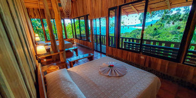 The rooms are elegant, breezy and comfortable, made from reforested 20 year old trees from our property. From their balcony, guests can enjoy the expansive view of the rainforest and the ocean overlooking the Marino Ballena National Park. The Deluxe Suites with ocean view are equipped with a living room and private bathroom (with solar heated water), ceiling fan, Wi-Fi access and security box with padlock. The local craftsmanship with wood, stone, shell and sand is unique..